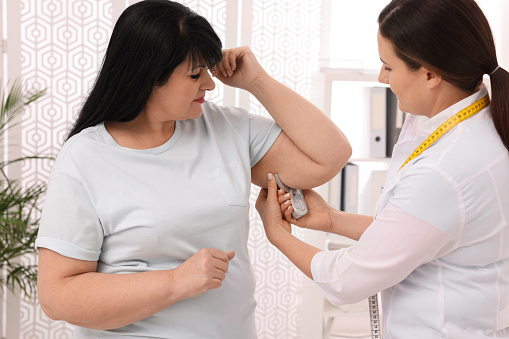 Nutritionist Measuring Overweight Woman's Body Fat Layer with Caliper in Clinic